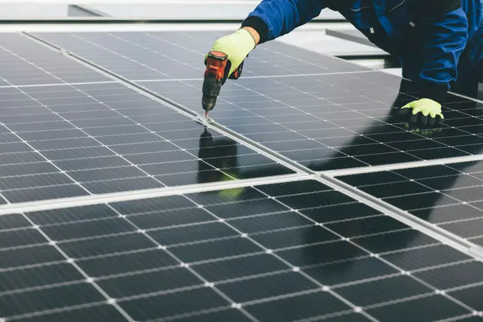 Mains gantées posant un module photovoltaïque sur une rangée déjà installée